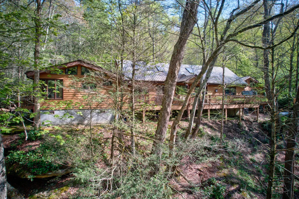 The wooden deck wraps around the house with large windows and trees in the background, merging interior and exterior living, and inviting exploration of nature trails just steps away.