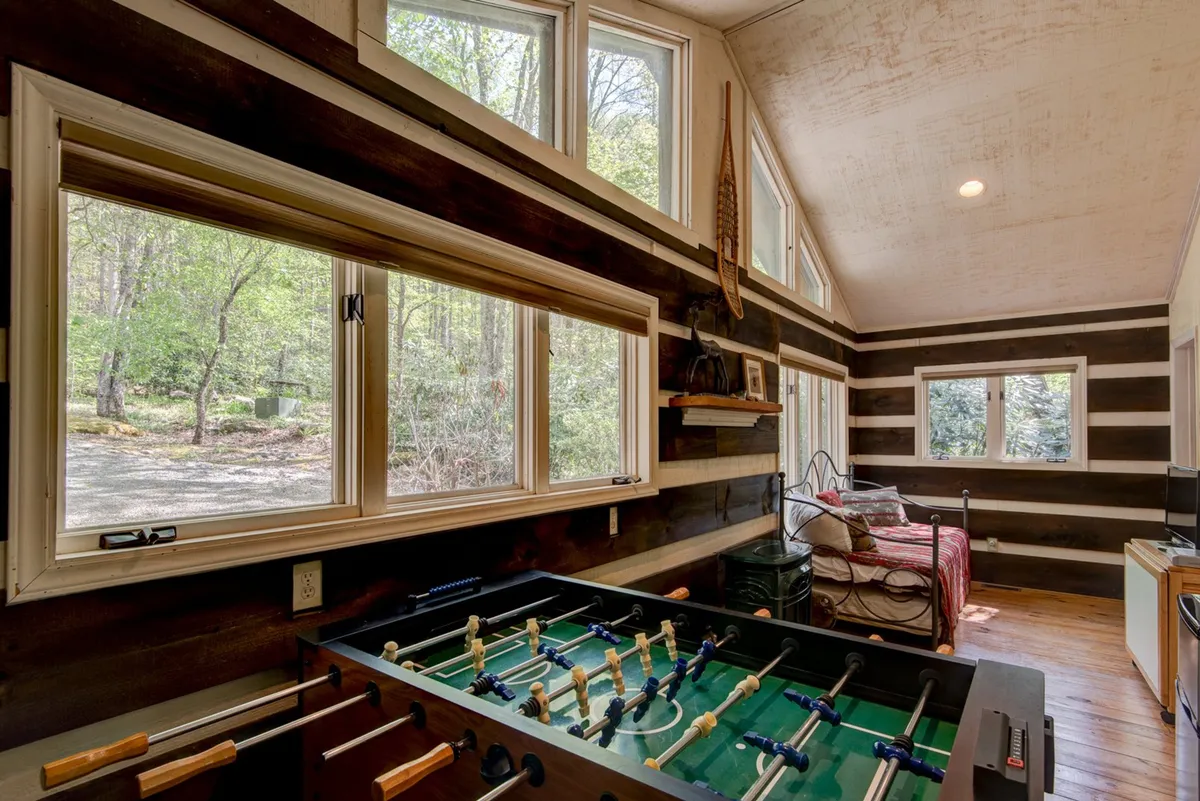 This image features a foosball table set next to large windows that let in natural light, surrounded by wooden walls and a cozy seating area. The playful and relaxed mood is emphasized by the inviting setup, perfect for group activities or friendly competition.