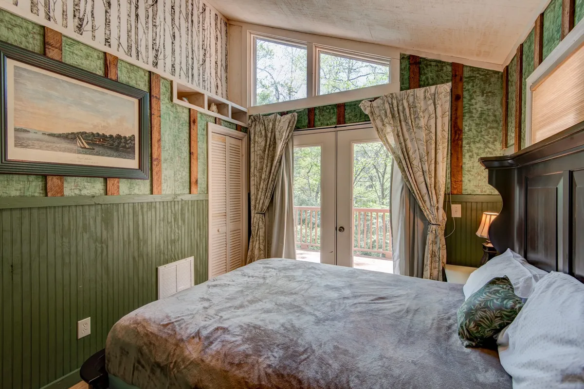 A tranquil bedroom featuring a comfortable bed, double doors that open directly onto a balcony, and tasteful wall artwork. The room is softly lit and emphasizes the blend of indoor comfort and outdoor access.