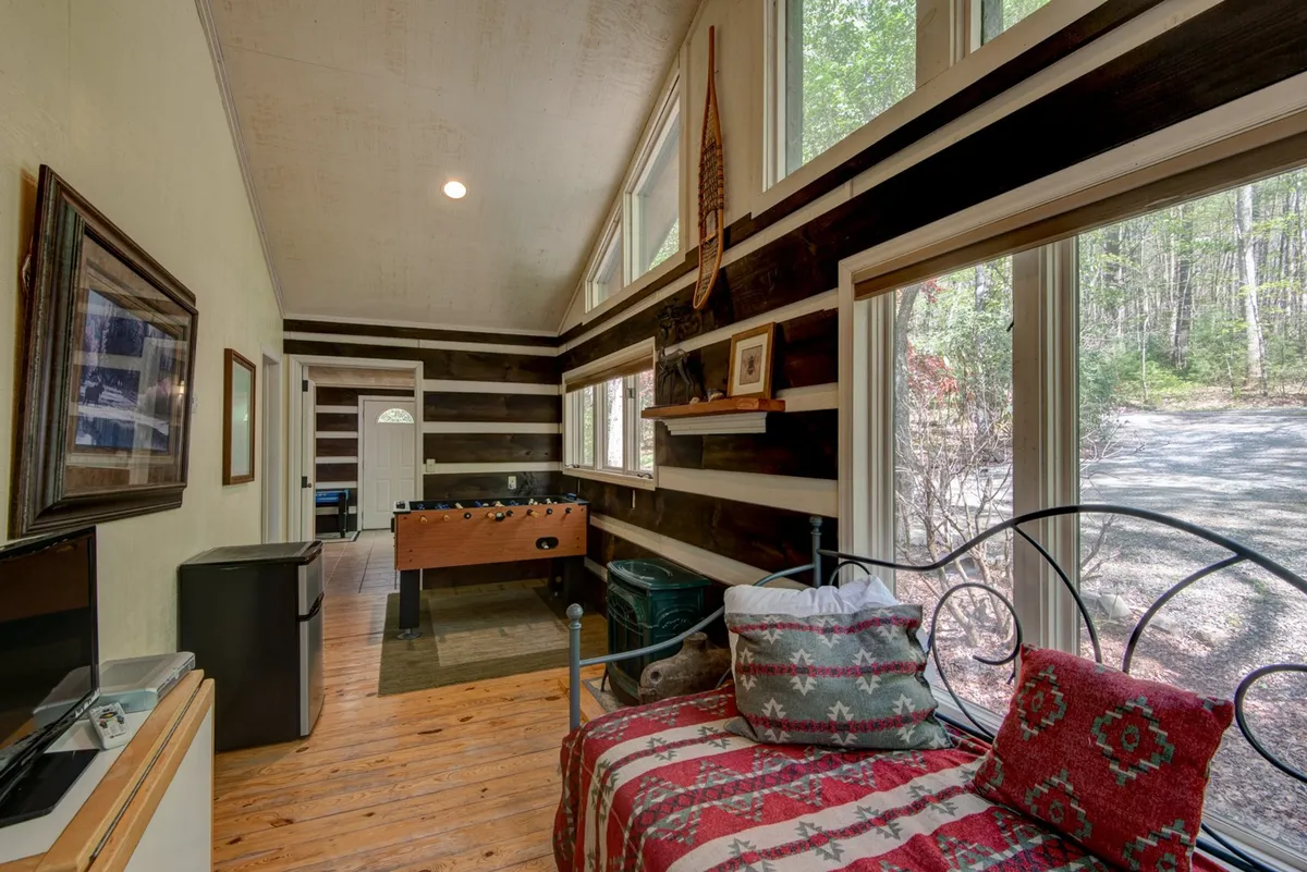 A flexible living space featuring a sofa bed with patterned pillows, a foosball table, and large windows letting in natural light. The room feels casual and adaptable, perfect for extra guests or playful family activities.