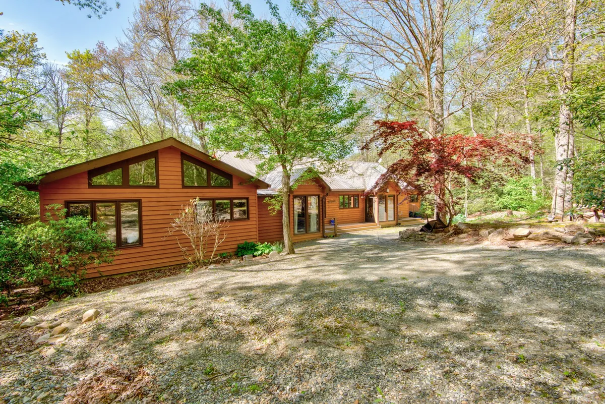 This exterior image features the wooden exterior of the house nestled amid lush greenery and vibrant, colorful trees, creating a tranquil and inviting mountain retreat feeling. The natural surroundings suggest seasonal changes, with a sense of both summer and fall beauty.